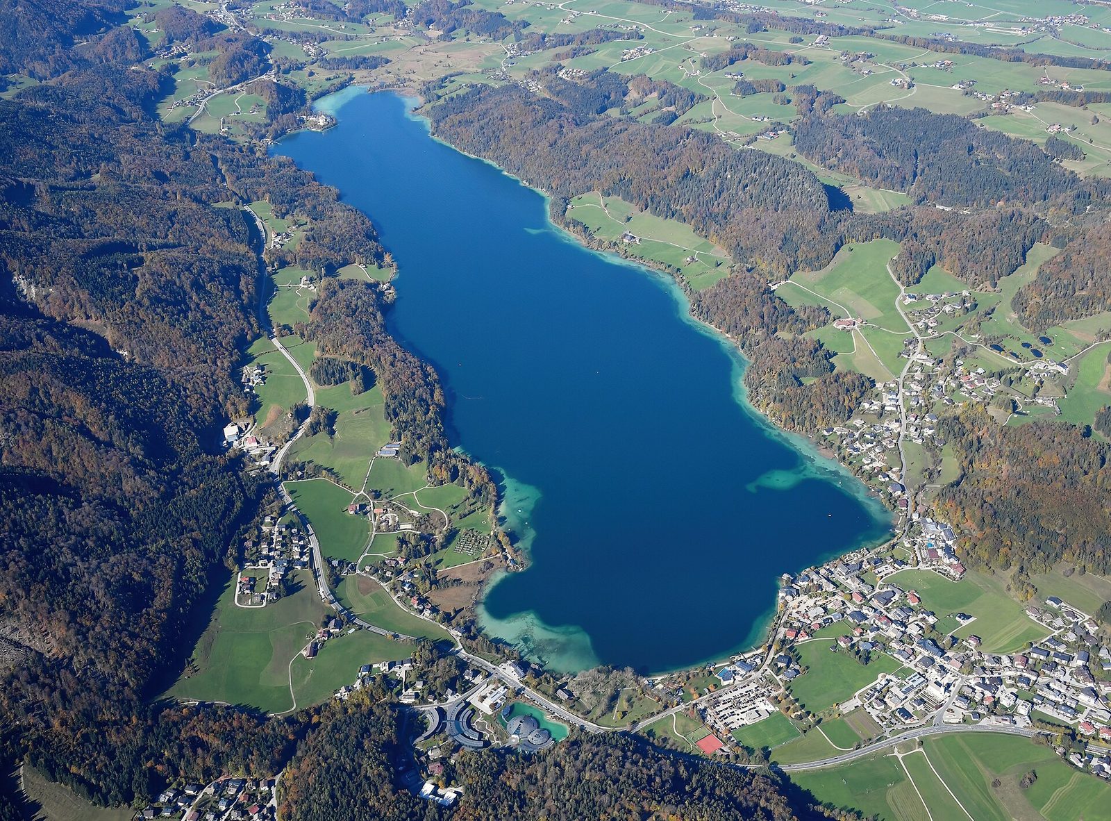 Der Fuschlsee im Salzkammergut aus der Luft, umgeben von goldbraunen Herbstwäldern