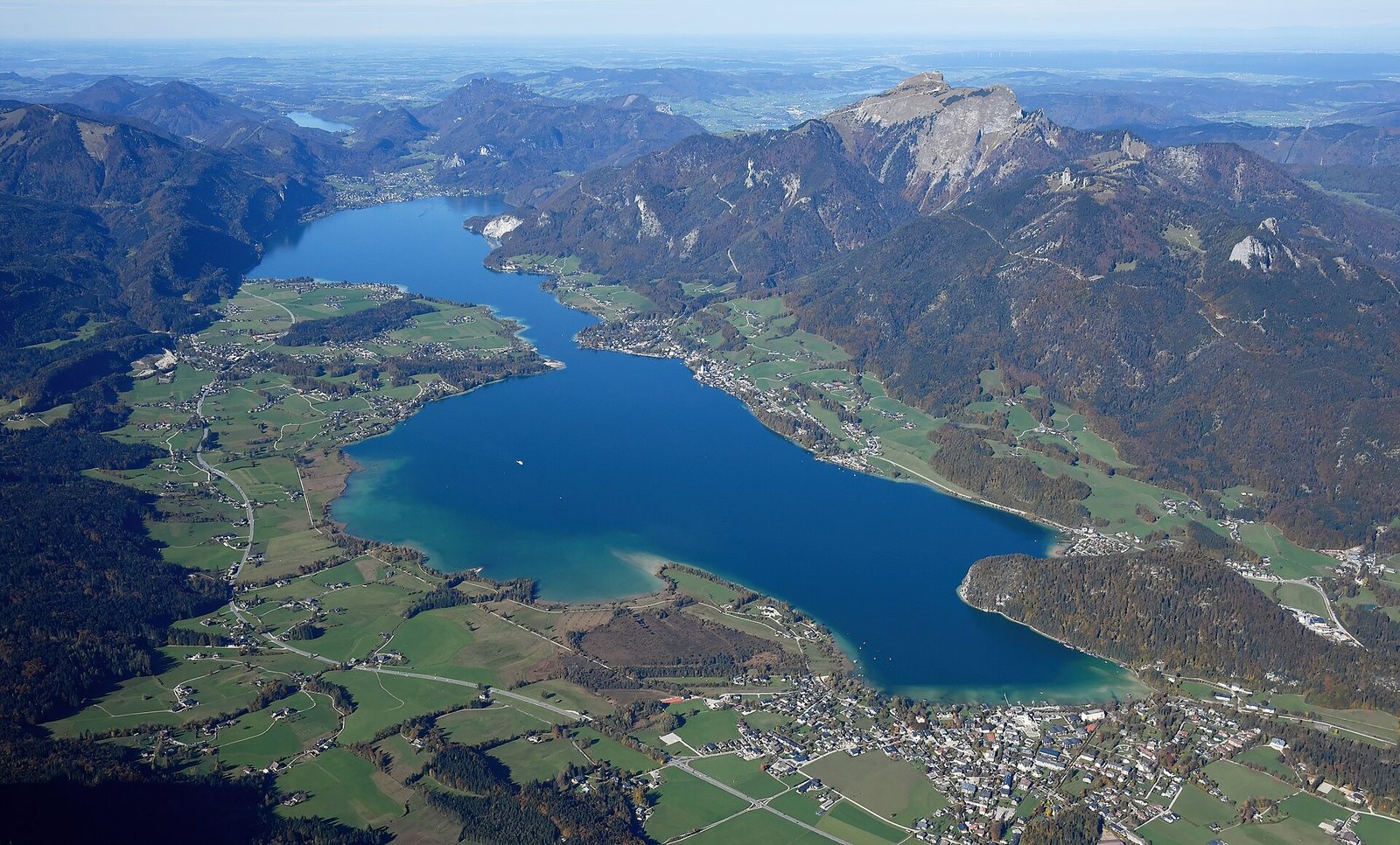 Der Wolfgangsee mit St. Gilgen aus der Luft, umgeben von herbstlichen Wäldern und Bergkämmen